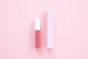 Elegant minimalist product shot of pink lip gloss with matching box on pastel background.